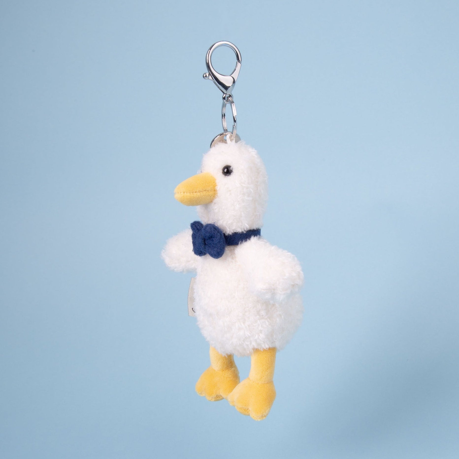 Plush duck keychain with a blue bow tie on a light blue background