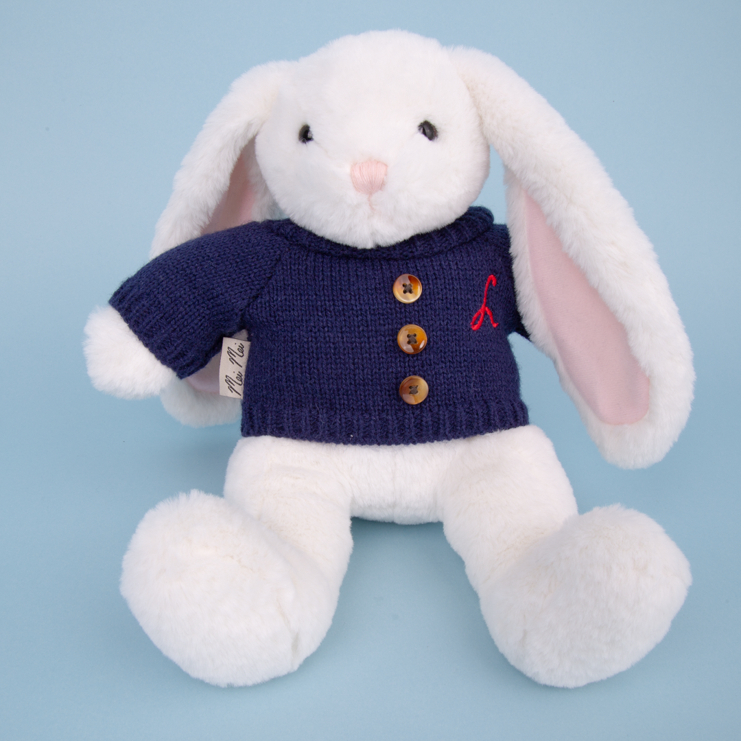 White plush bunny toy wearing a navy sweater with buttons on a light blue background