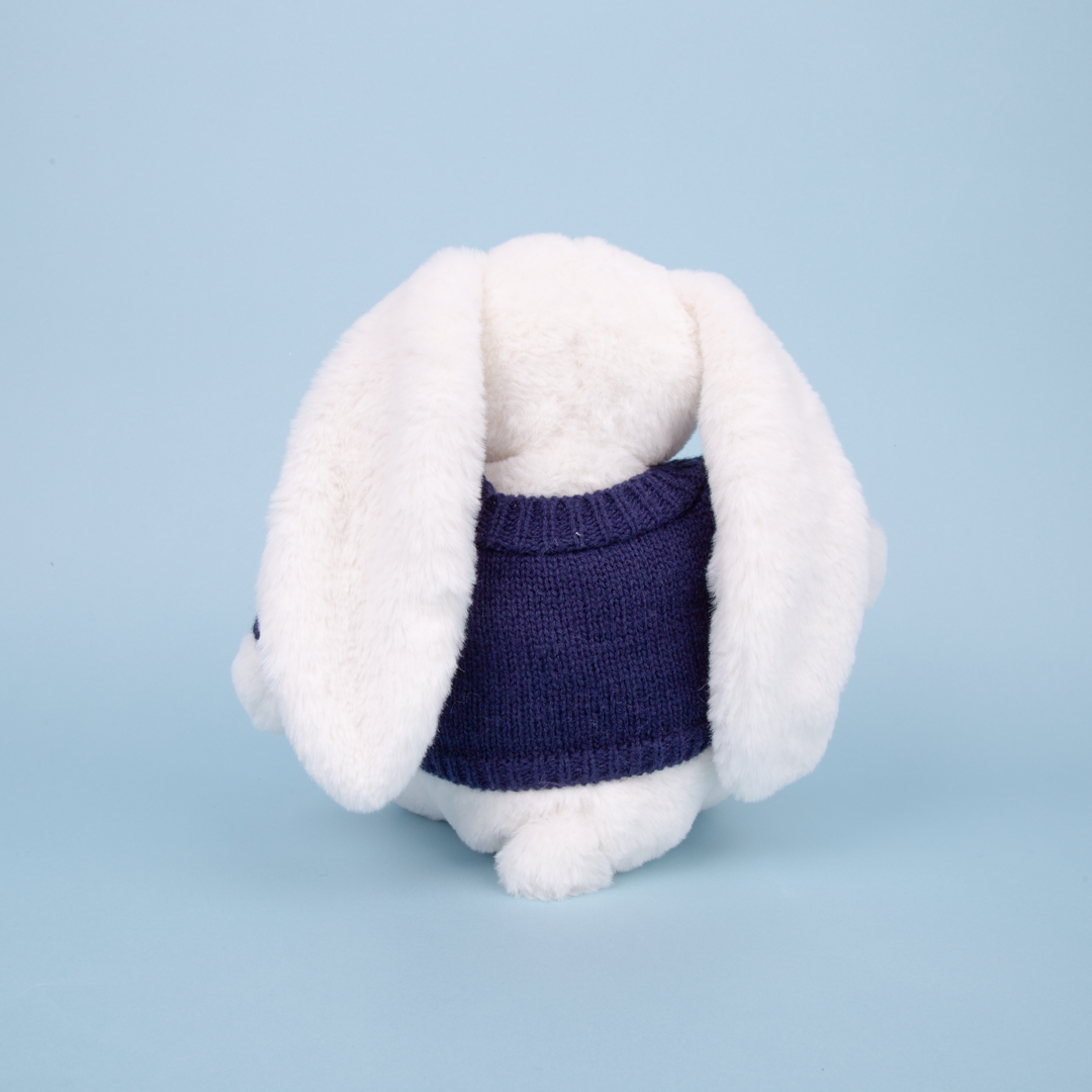 White plush toy rabbit wearing a navy blue sweater on a light blue background
