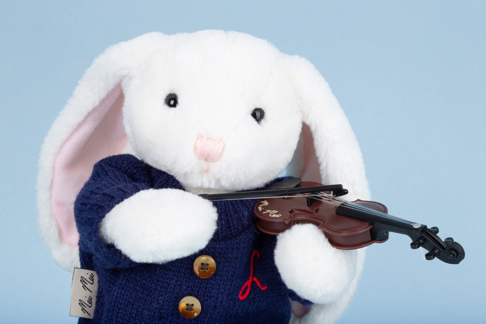 White plush bunny toy in a blue sweater holding a violin against a light blue background