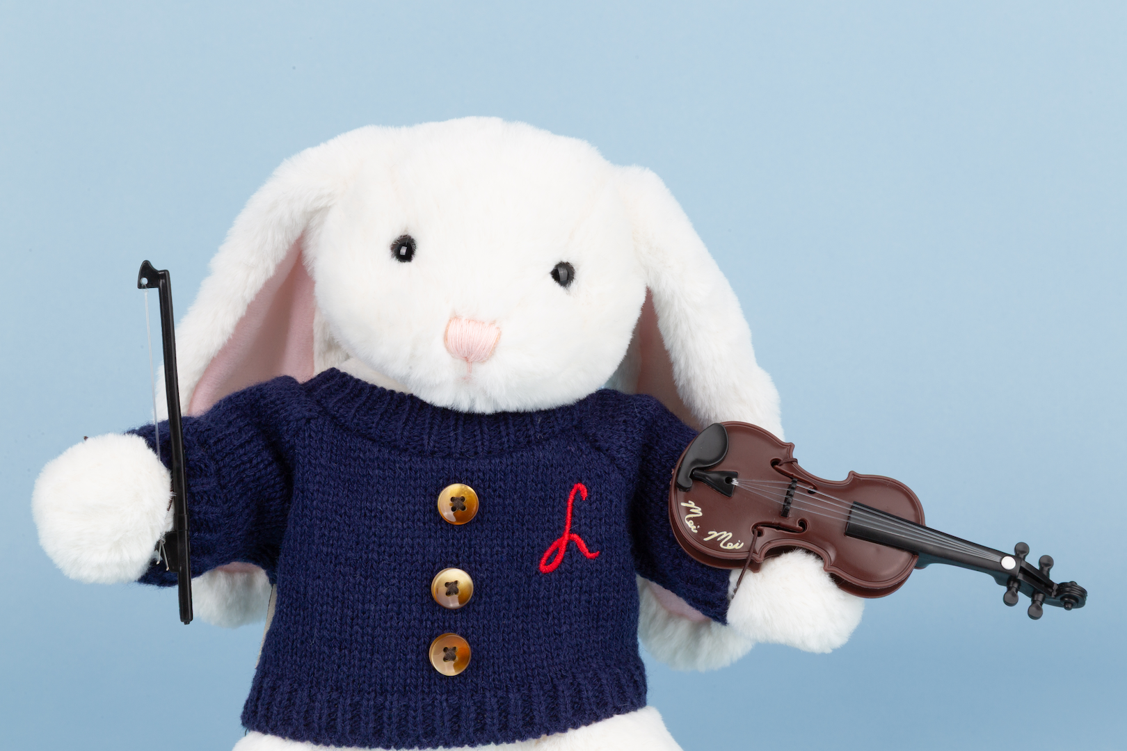 White rabbit plush toy wearing a navy sweater with gold buttons and a red letter 'L', holding a violin.